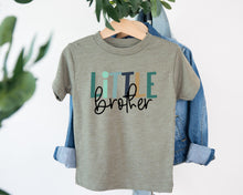 Load image into Gallery viewer, A gray t-shirt with the text "Little Brother" printed on it, hanging on a wooden hanger.