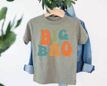 Load image into Gallery viewer, A gray t-shirt with the text "BIG BRO" printed in orange and teal colors, hanging on a clothing hanger.