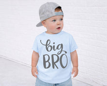 Load image into Gallery viewer, A young child wearing a gray baseball cap and a light blue t-shirt with the text "big bro" printed on it, standing in front of a white brick wall.