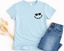 Load image into Gallery viewer, A light blue t-shirt with a graphic design and text, along with a pair of blue jeans, are displayed on a white background.