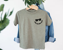 Load image into Gallery viewer, A gray t-shirt with a graphic design and text printed on it, hanging on a clothing hanger.