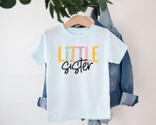 Load image into Gallery viewer, A white t-shirt with the text "LITTLE SISTER" printed on it, hanging on a clothing hanger.