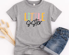 Load image into Gallery viewer, A gray t-shirt with the text "LITTLE Sister" printed on it, along with a pair of blue jeans.