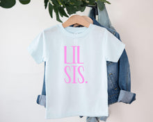 Load image into Gallery viewer, A light blue t-shirt with the text "LIL SIS" printed in pink on it, hanging on a wooden hanger.