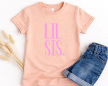 Load image into Gallery viewer, A pink t-shirt with the text "LIL SIS" printed on it, along with a pair of blue denim shorts, are laid out on a white background.