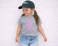 Load image into Gallery viewer, A young girl wearing a green baseball cap and a gray t-shirt with pink text stands against a white brick wall.