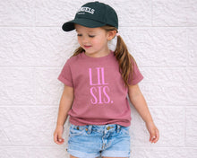 Load image into Gallery viewer, A young girl wearing a green baseball cap and a pink t-shirt with the text "LIL SIS." stands against a white brick wall.
