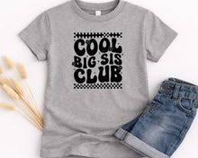 Load image into Gallery viewer, A gray t-shirt with the text "COOL BIG SIS CLUB" printed on it, along with a pair of blue jeans.