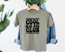 Load image into Gallery viewer, A gray t-shirt with the text "COOL BIG SIS CLUB" printed on it, hanging on a clothing hanger.