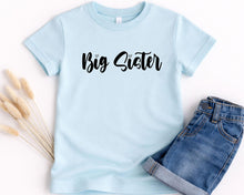 Load image into Gallery viewer, A light blue t-shirt with the text "Big Sister" printed on it, along with a pair of denim shorts.