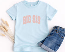 Load image into Gallery viewer, A light blue t-shirt with the text "BIG SIS" printed on it, along with a pair of denim shorts, are displayed on a white background.