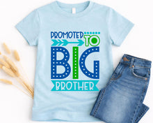 Load image into Gallery viewer, A light blue t-shirt with a graphic design that says "PROMOTED TO BIG BROTHER" in blue and green text, along with an arrow pointing to the word "BIG". The t-shirt is placed next to a pair of blue jeans.