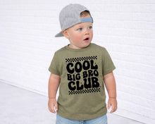 Load image into Gallery viewer, A young child wearing a green t-shirt with the text "COOL BIG BRO CLUB" printed on it, along with a gray baseball cap.