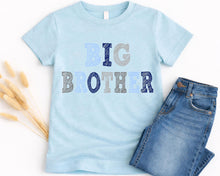 Load image into Gallery viewer, A light blue t-shirt with the text "BIG BROTHER" printed on it, along with a pair of blue jeans.