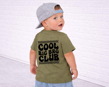 Load image into Gallery viewer, A young child wearing a green t-shirt with the text "COOL BIG BRO CLUB" printed on the back, standing in front of a white brick wall.