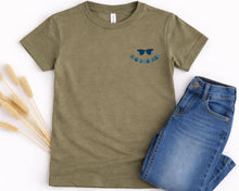Load image into Gallery viewer, A green t-shirt with a pair of blue jeans and a pair of sunglasses on it, along with some dried flowers.