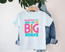 Load image into Gallery viewer, A white t-shirt with a colorful graphic design that says "Promoted to Big Sister" hanging on a wooden hanger.
