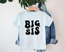 Load image into Gallery viewer, A white t-shirt with the text "BIG SIS" printed on it, hanging on a clothing hanger.