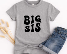 Load image into Gallery viewer, A gray t-shirt with the text "BIG SIS" printed on it, along with a pair of blue jeans.