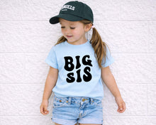 Load image into Gallery viewer, A young girl wearing a blue t-shirt with the text "BIG SIS" and a black baseball cap stands against a white wall.