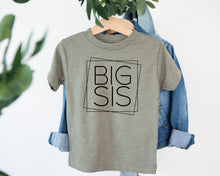 Load image into Gallery viewer, A gray t-shirt with the text "BIG SIS" printed on it, hanging on a wooden hanger.