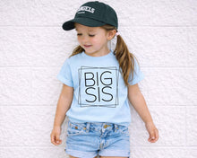 Load image into Gallery viewer, A young girl wearing a blue t-shirt with the text "BIG SIS" and a black baseball cap stands against a white brick wall.