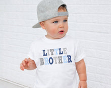 Load image into Gallery viewer, A young child wearing a gray baseball cap and a white t-shirt with the text "Little Brother" printed on it.
