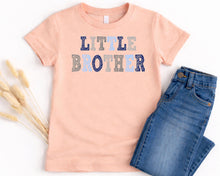 Load image into Gallery viewer, A peach-colored t-shirt with the text "LITTLE BROTHER" printed on it, along with a pair of blue jeans.
