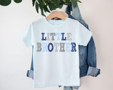 Load image into Gallery viewer, A light blue t-shirt with the text "LITTLE BROTHER" printed on it, hanging on a clothing hanger.
