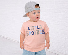 Load image into Gallery viewer, A young child wearing a gray baseball cap and a pink t-shirt with the text "Little Brother" printed on it, standing in front of a white brick wall.
