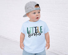 Load image into Gallery viewer, A young child wearing a gray baseball cap and a light blue t-shirt with the text "Little brother" printed on it, standing in front of a white brick wall.
