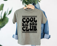 Load image into Gallery viewer, A gray t-shirt with the text "COOL BIG BRO CLUB" printed on it, hanging on a wooden hanger.
