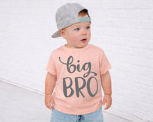 Load image into Gallery viewer, A young child wearing a gray cap and a pink t-shirt with the text "big bro" stands in front of a white brick wall.
