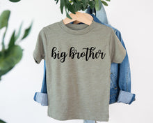 Load image into Gallery viewer, A gray t-shirt with the text "big brother" printed on it, hanging on a wooden hanger.
