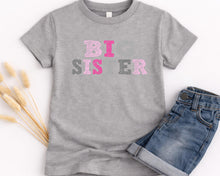Load image into Gallery viewer, A gray t-shirt with the text "BIG SISTER" printed on it, along with a pair of blue jeans.
