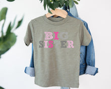 Load image into Gallery viewer, A gray t-shirt with the text "BIG SISTER" printed on it, hanging on a clothing hanger.
