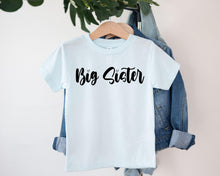 Load image into Gallery viewer, A white t-shirt with the text "Big Sister" printed on it, hanging on a clothing hanger.
