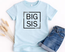 Load image into Gallery viewer, A light blue t-shirt with the text "BIG SIS" printed on it, along with a pair of denim shorts.
