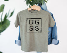 Load image into Gallery viewer, A gray t-shirt with the text "BIG SIS" printed on it, hanging on a wooden hanger.
