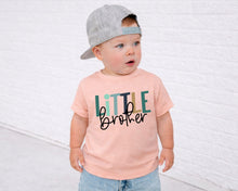 Load image into Gallery viewer, A young child wearing a gray baseball cap and a pink t-shirt with the text "Little Brother" printed on it, standing in front of a white brick wall.

