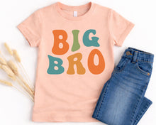 Load image into Gallery viewer, A pink t-shirt with the text "BIG BRO" printed on it, along with a pair of blue jeans.
