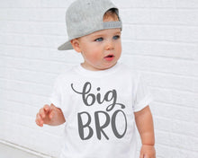 Load image into Gallery viewer, A young child wearing a white t-shirt with the text "big bro" printed on it, standing in front of a white brick wall.
