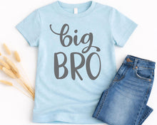 Load image into Gallery viewer, A light blue t-shirt with the text "BIG BRO" printed on it, along with a pair of blue jeans and some dried flowers.
