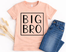 Load image into Gallery viewer, A pink t-shirt with the text "BIG BRO" printed on it, along with a pair of blue jeans, are displayed on a white background.
