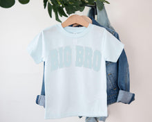 Load image into Gallery viewer, A light blue t-shirt with the text "BIG BRO" printed on it, hanging on a wooden hanger.
