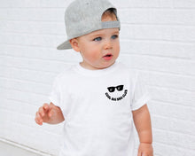 Load image into Gallery viewer, A young child wearing a white t-shirt with a graphic and text printed on it, standing in front of a white brick wall.
