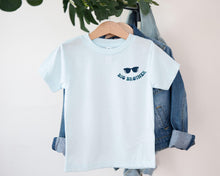 Load image into Gallery viewer, A light blue t-shirt with a graphic design and text, hanging on a clothing hanger.
