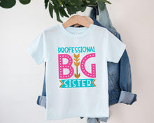 Load image into Gallery viewer, A white t-shirt with a graphic design that says "PROFESSIONAL BIG SISTER" in pink and teal colors, hanging on a clothing hanger.
