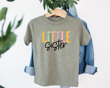 Load image into Gallery viewer, A gray t-shirt with the text "LITTLE Sister" printed on it, hanging on a clothing hanger.
