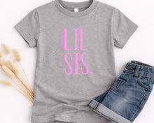 Load image into Gallery viewer, A gray t-shirt with the text "LIL SIS" in pink letters, along with a pair of blue denim shorts, are displayed on a white background.
